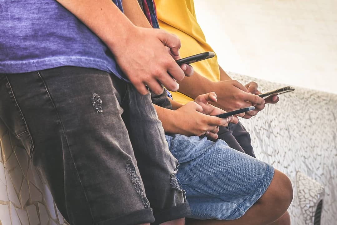 A group of teenagers using their smartphones outdoors.